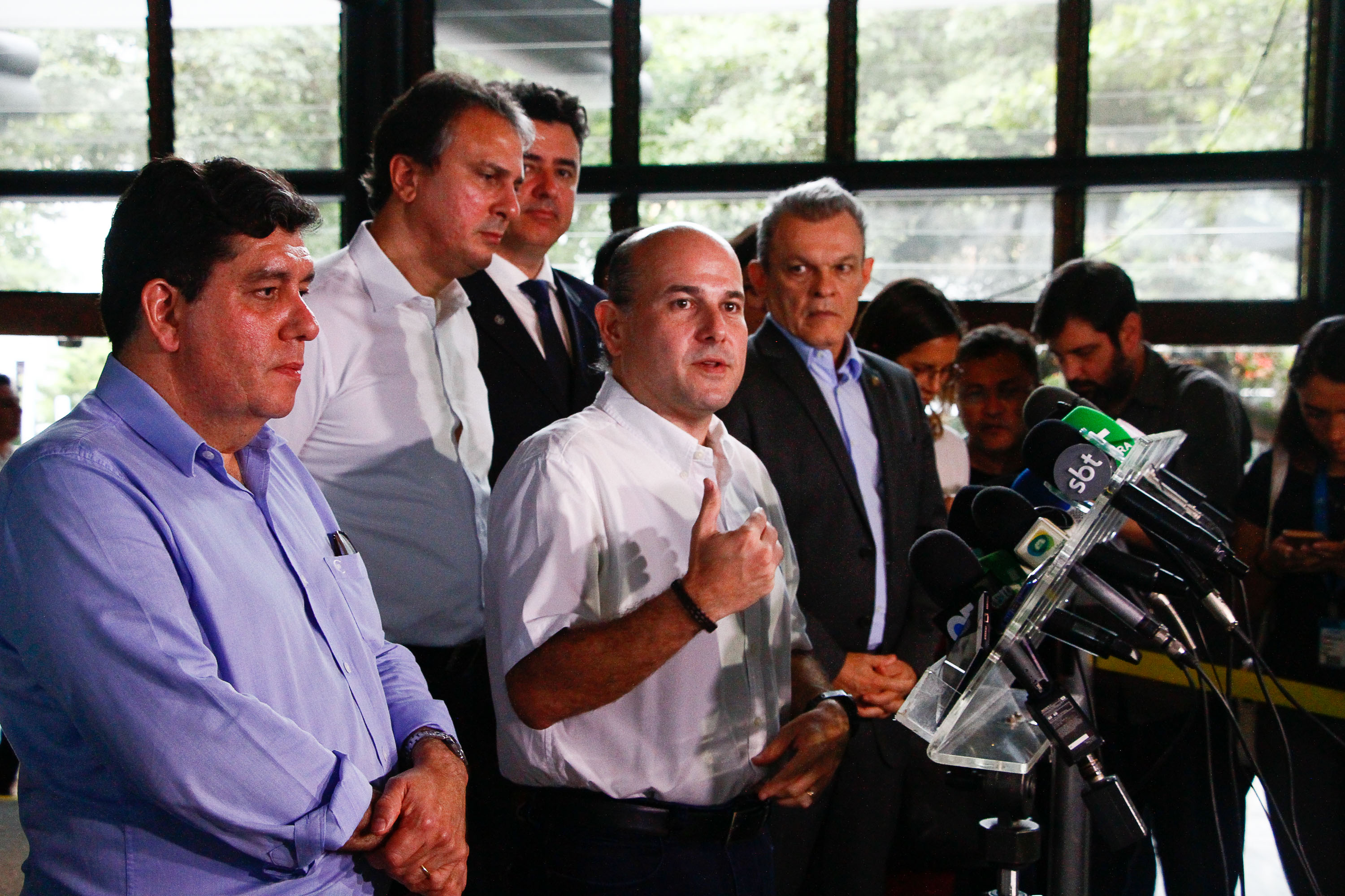 prefeito falando em frente à vários microfones com governador e secretários em pé atrás